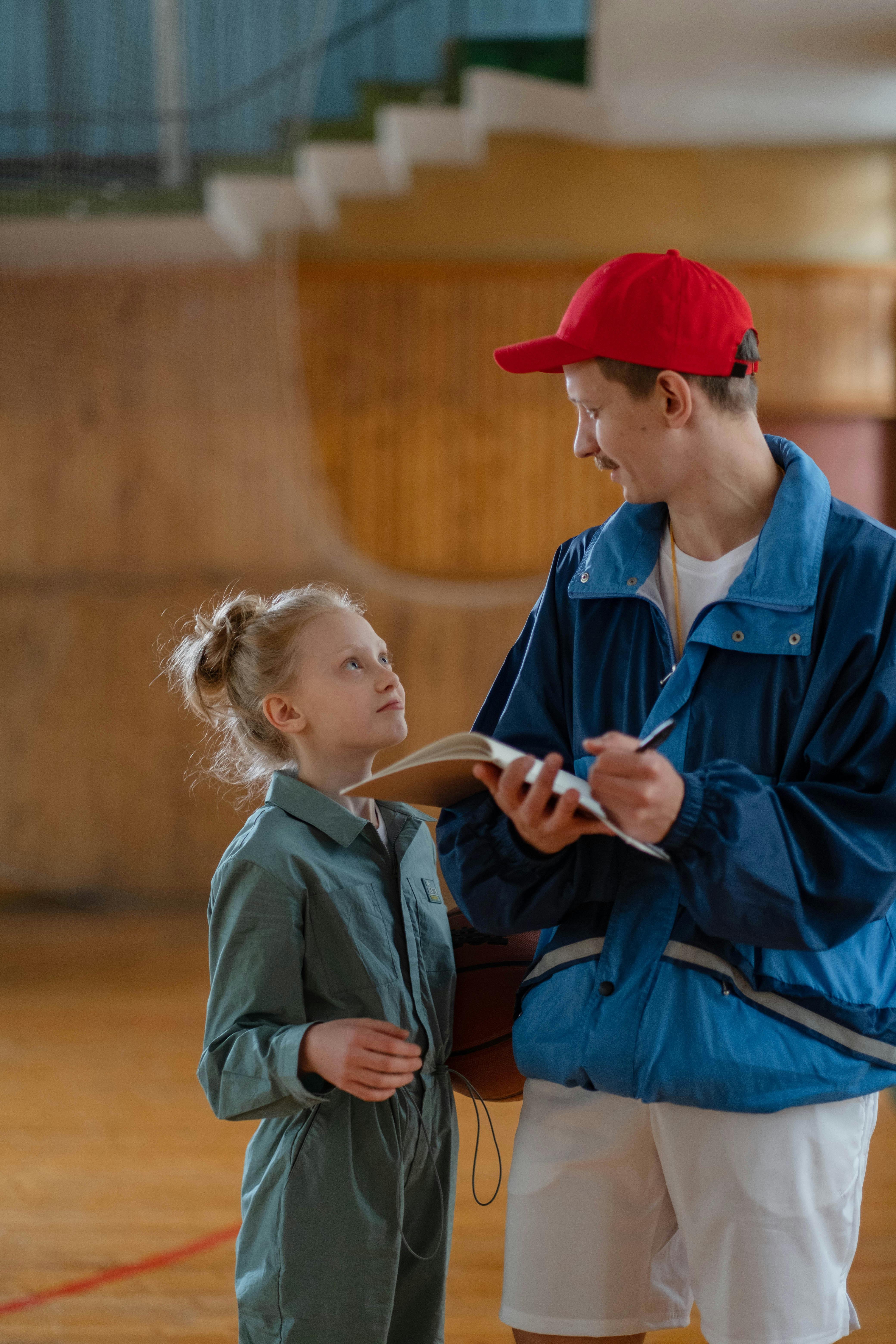 PE coach with clipboard supporting primary school pupil in sports hall